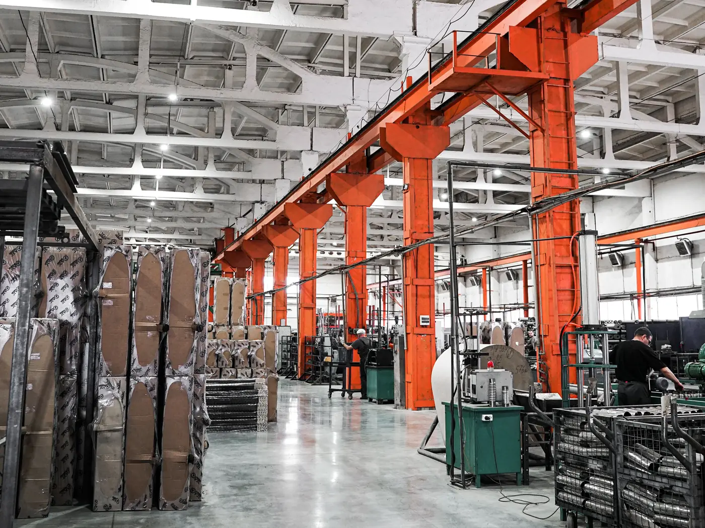 Hall de production industriel aux piliers orange, avec des opérateurs aux machines